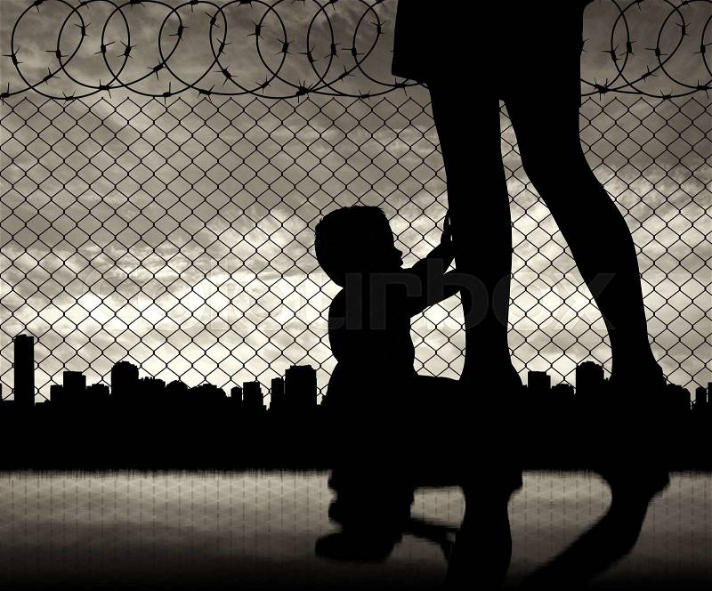Refugee family concept. Silhouette of the child and refugee mothers legs near the border on the background of the urban landscape, stock photo