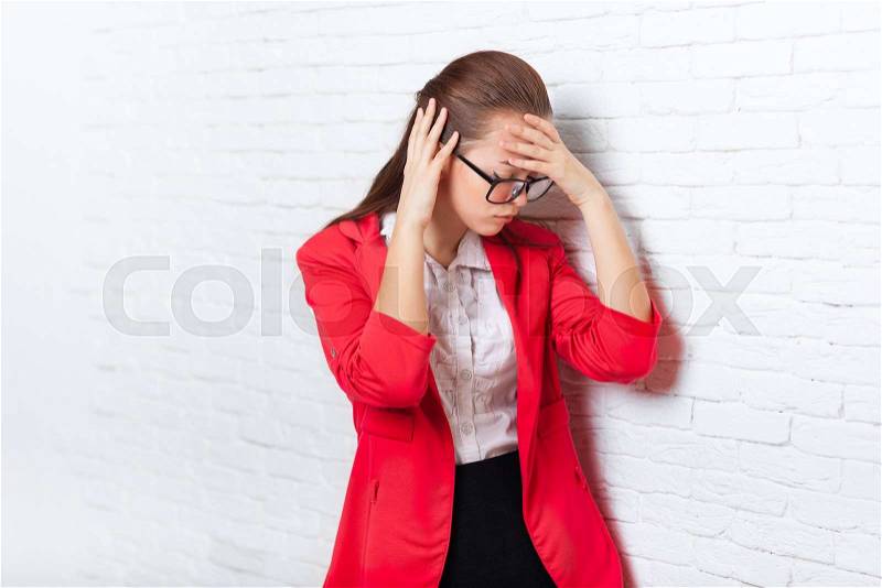 Businesswoman hold hands on head, ache, pain depressed wear red jacket glasses stressed business woman over office wall, stock photo