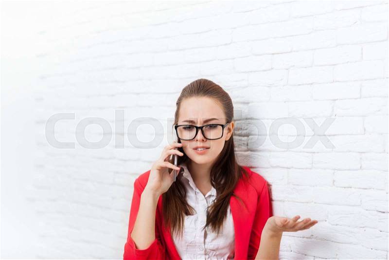 Businesswoman serious negative cell phone call problem wear red jacket glasses talking on mobile business woman over office wall, stock photo