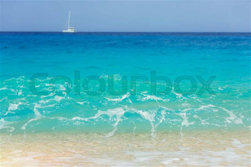 Turquoise blue water with foamy waves and yacht on horizon, stock photo