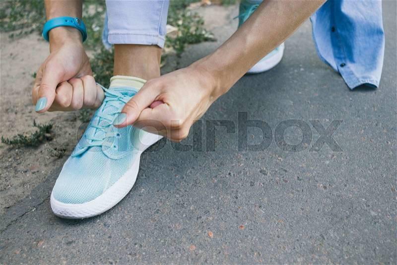Close-up of girl ties the laces on the shoes while walking around the city, stock photo