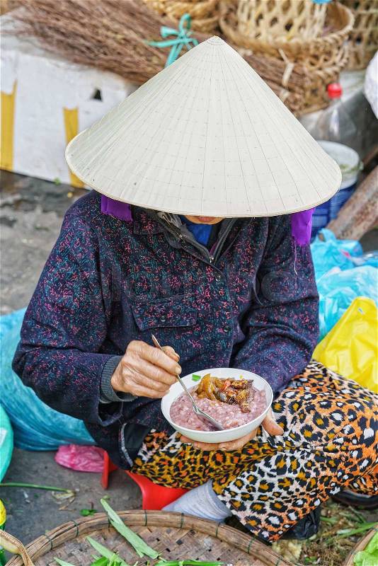 Asian woman in traditional Vietnamese hat eating food in the street market in Hoi An, Vietnam. No face, stock photo