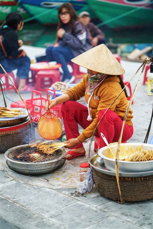 Hoi An, Vietnam - February 17, 2016: Asian woman in traditional Vietnamese hat cooking chicken paws for selling in the street market in Hoi An, Vietnam, stock photo
