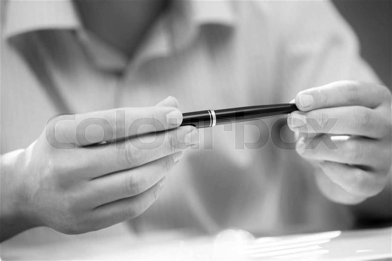 Man\'s hands holding a black pen in both arms in a thinking gesture during a meeting or negotiation. Black and white image, stock photo