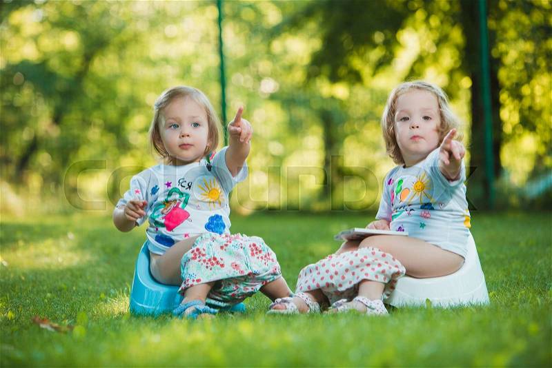 The two little baby girls two-year old hanging upside down against green grass, stock photo