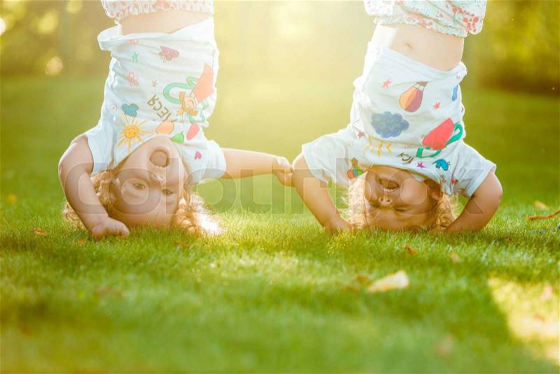 The two little baby girls two-year old hanging upside down against green grass, stock photo