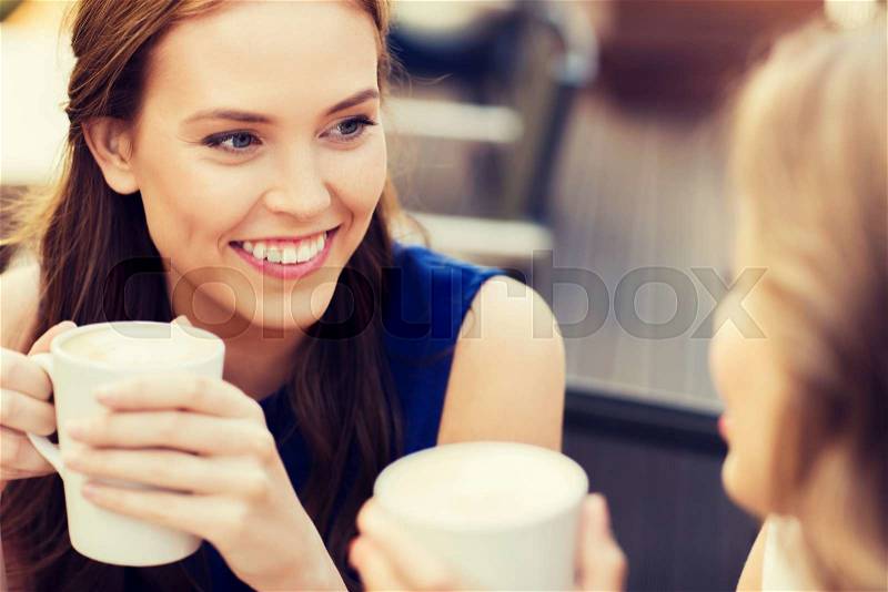 Communication and friendship concept - smiling young women with coffee cups at cafe, stock photo