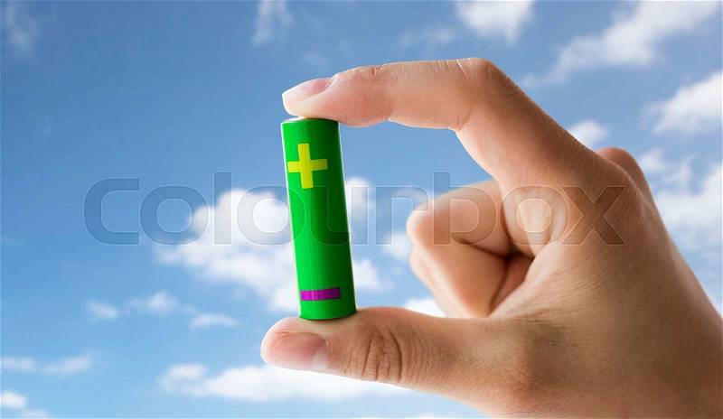Recycling, energy, power, environment and ecology concept - close up of hand holding green alkaline battery over blue sky and clouds background, stock photo