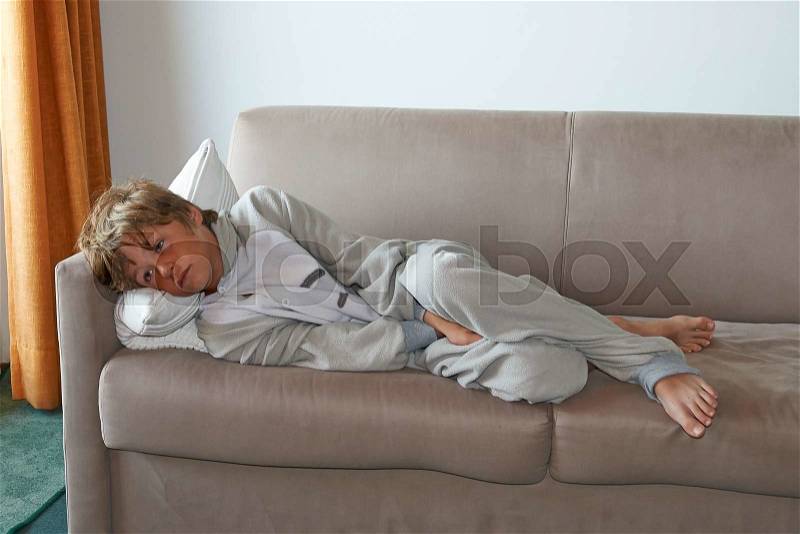 Young boy tired watch television program on sofa, stock photo
