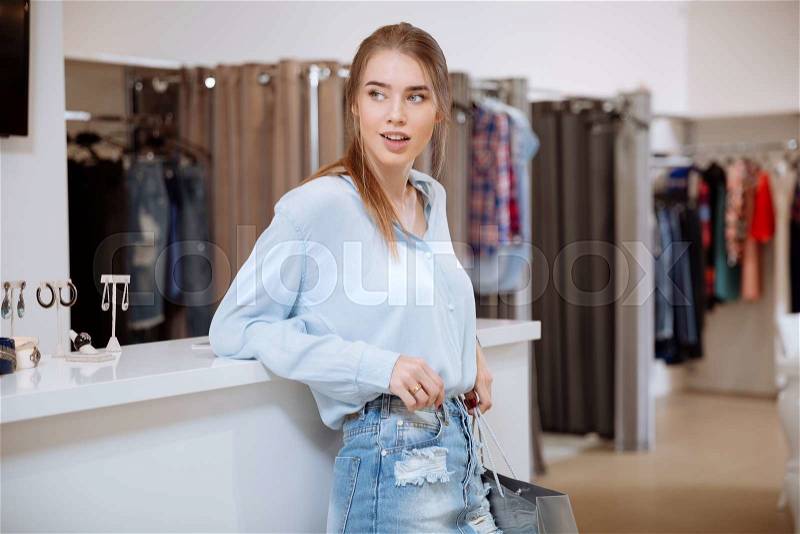 Relaxed happy young woman with shopping bag standing in clothing store, stock photo