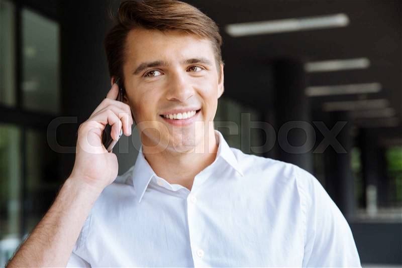 Happy businessman in white shirt talking on cell phone outdoors, stock photo