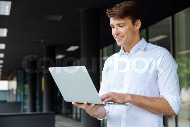 Cheerful businessman standing and using laptop, stock photo