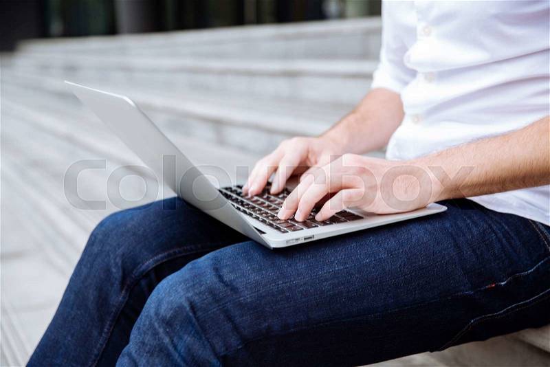 Young man sitting on stairs and using laptop, stock photo