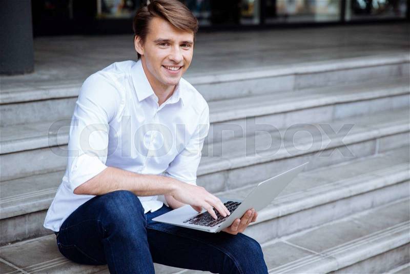 Happy man sitting outdoors and using laptop, stock photo