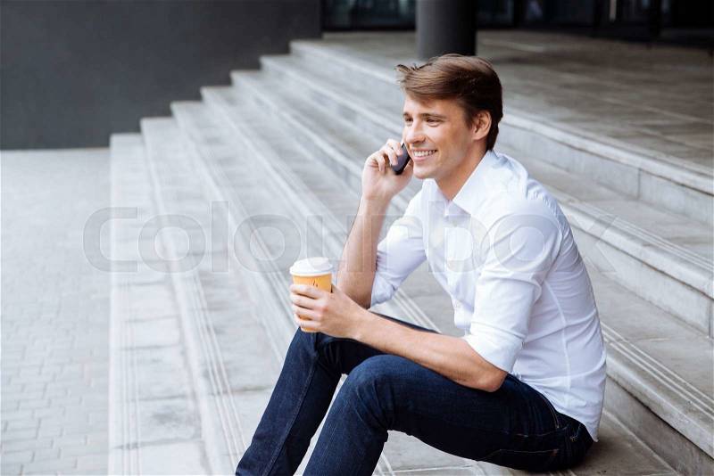 Cheerful businessman with cup of coffee talking on mobile phone, stock photo