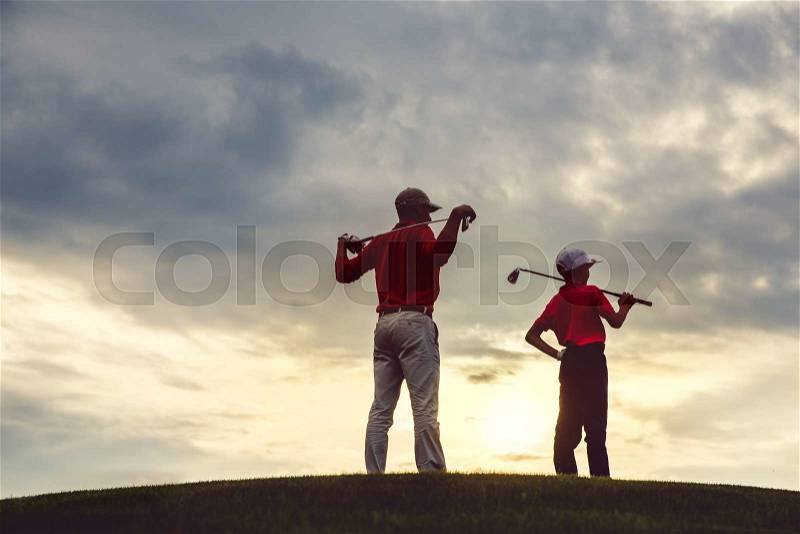Man with his son golfers standing on golf course at sunset, back view, stock photo