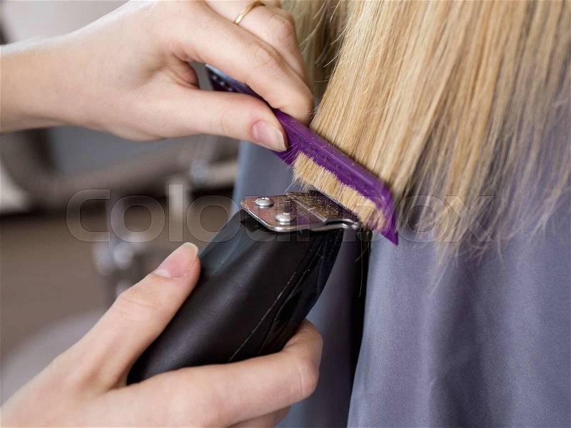 Hairstyle. Close up barber\'s hands trimming the ends of long blonde hair with the machine and the comb, stock photo