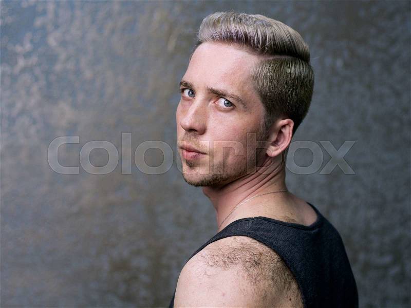 Man\'s hairstyle. Close up portrait of a young blonde man, face is half turned, gray background , stock photo