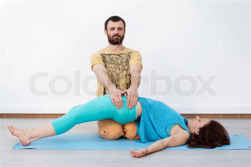 Pair exercises. Massage. Man performing thai massage, presses on her buttock, woman is laying on the mat relaxing, stock photo