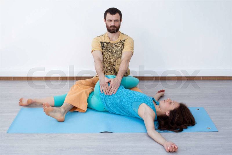 Pair exercises. Stretching. Man performing thai massage, srtetching woman\'s legs, woman is laying on the mat relaxing, stock photo