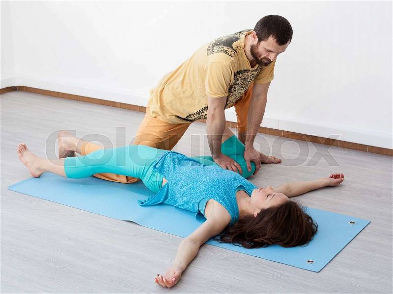 Pair exercises. Stretching. Man performing thai massage, srtetching woman\'s legs, woman is laying on the mat relaxing, stock photo