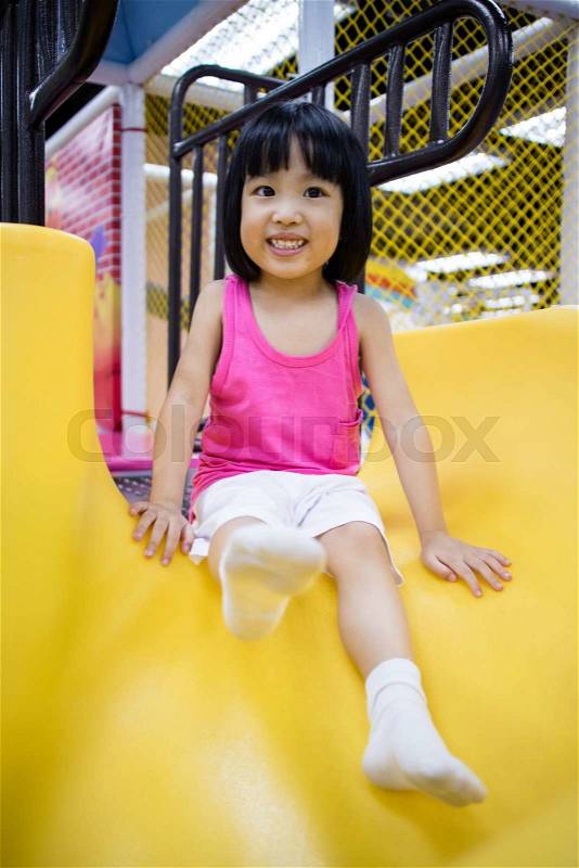 Asian Chinese Little Girl Playing on the Slide at Indoor Colourful Playground, stock photo