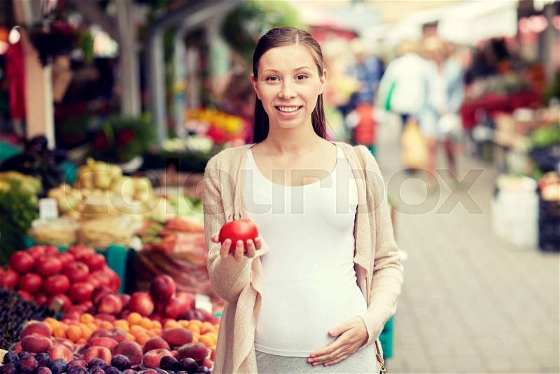 Sale, shopping, food, pregnancy and people concept - happy pregnant woman holding tomato at street market, stock photo