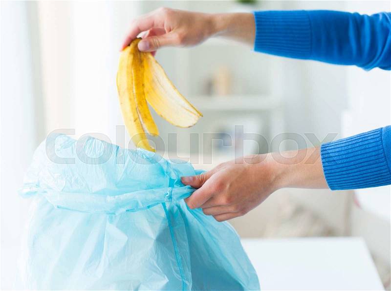 Recycling, food waste, garbage, environment and ecology concept - close up of hand putting banana peel into rubbish bag at home, stock photo