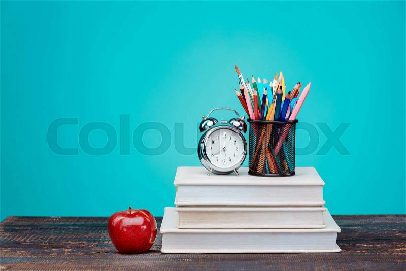 Back to School concept.School Books, colored pencils and clock on blue background, stock photo