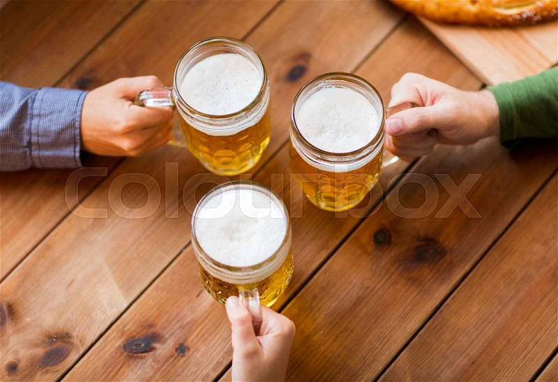 People, leisure and drinks concept - close up of male hands with beer mugs at bar or pub, stock photo