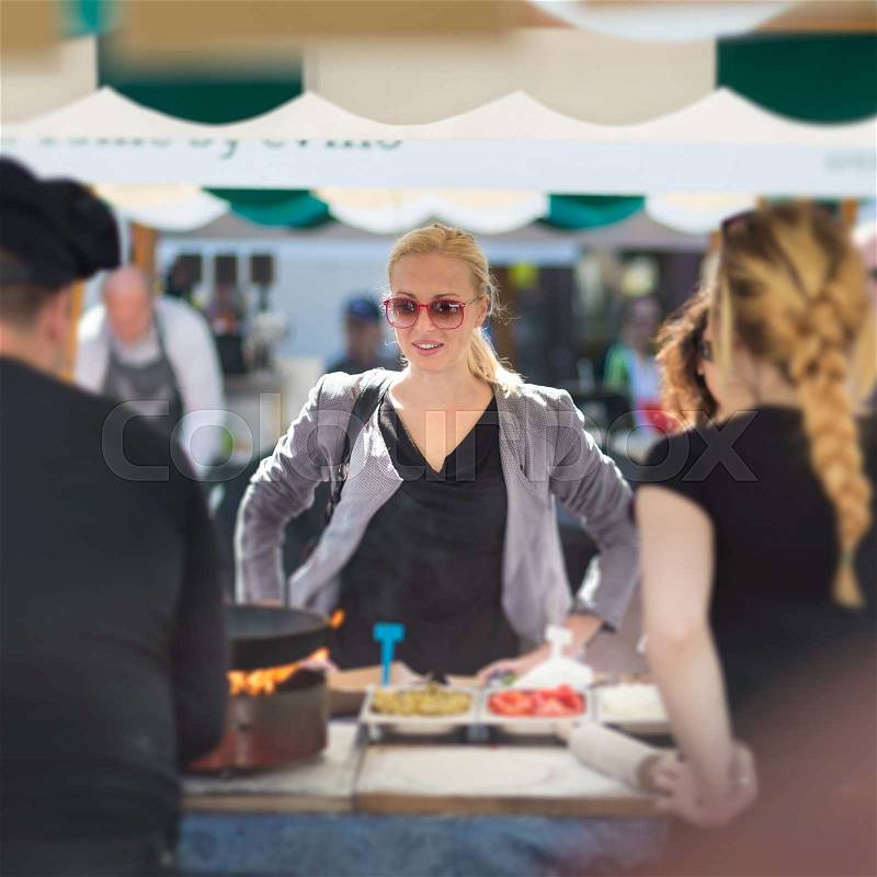 Beautiful blonde caucasian lady buying freshly prepared meal at a local street food festival. Urban international kitchen event in Ljubljana, Slovenia, in summertime, stock photo