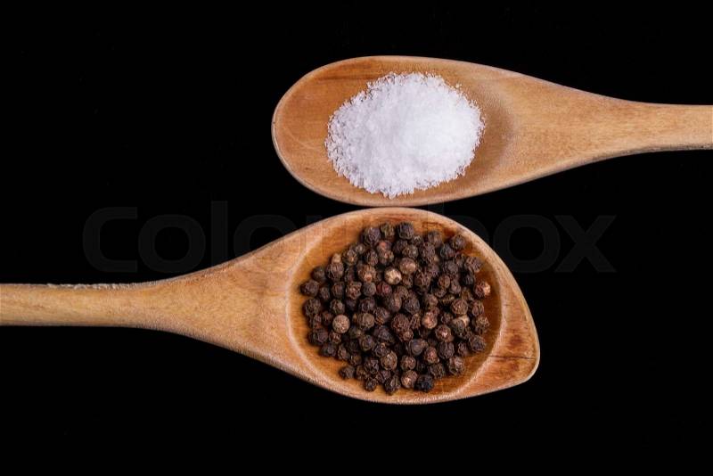 Salt and pepper corns on wooden spoons on a black background, stock photo