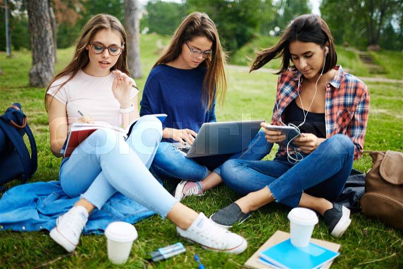 Three teenage girls carrying out home assignment in park, stock photo
