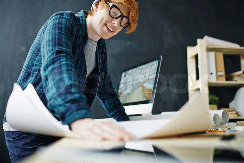 Creative designer looking at blueprint at workplace, stock photo