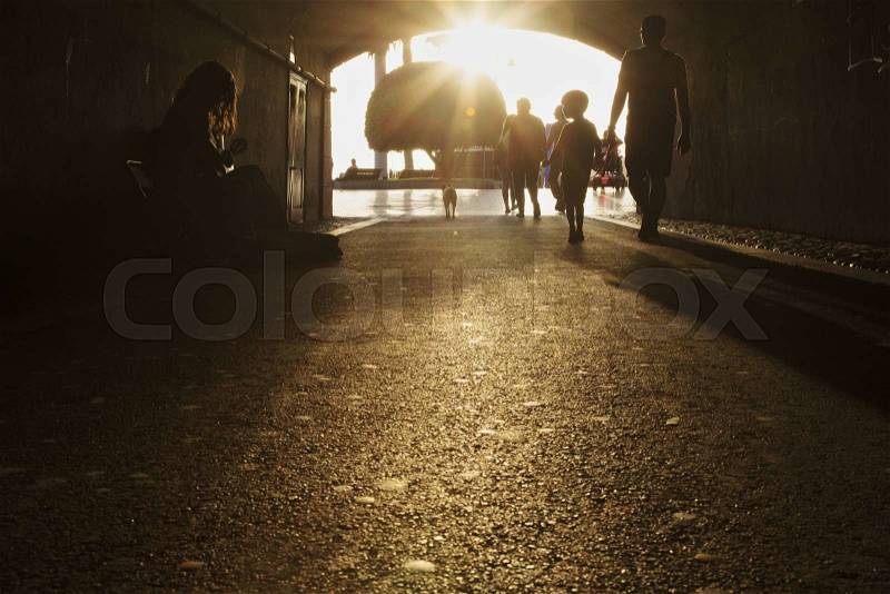 Outlines of humans passing by street artist in tunnel, stock photo
