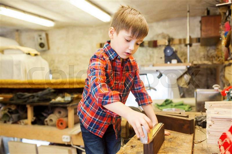 Children, profession, carpentry, woodwork and people concept - happy little boy with ruler measuring wood plank at workshop, stock photo