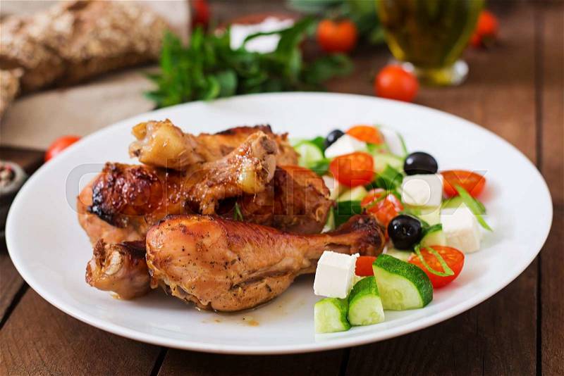 Appetizing oven baked golden chicken drumsticks and Greek salad, stock photo