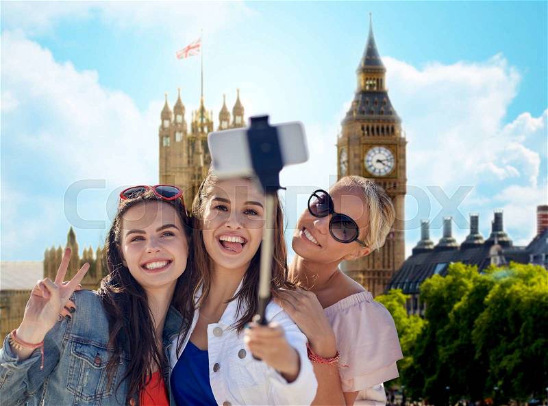 Summer vacation, holidays, travel, technology and people concept- group of smiling young women taking picture with smartphone on selfie stick over london city and big ben tower background, stock photo