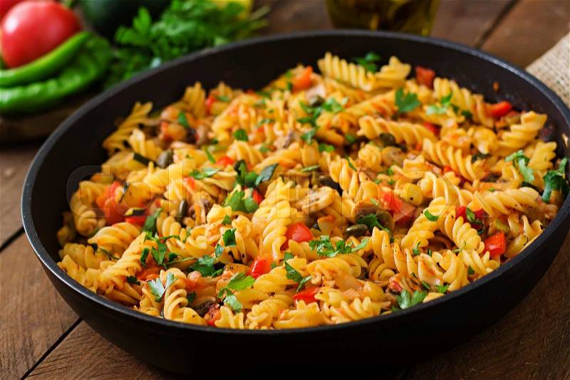 Vegetarian Vegetable pasta Fusilli with zucchini, mushrooms and capers in pan on wooden table, stock photo