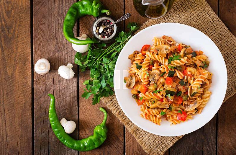 Vegetarian Vegetable pasta Fusilli with zucchini, mushrooms and capers in white bowl on wooden table. Top view, stock photo