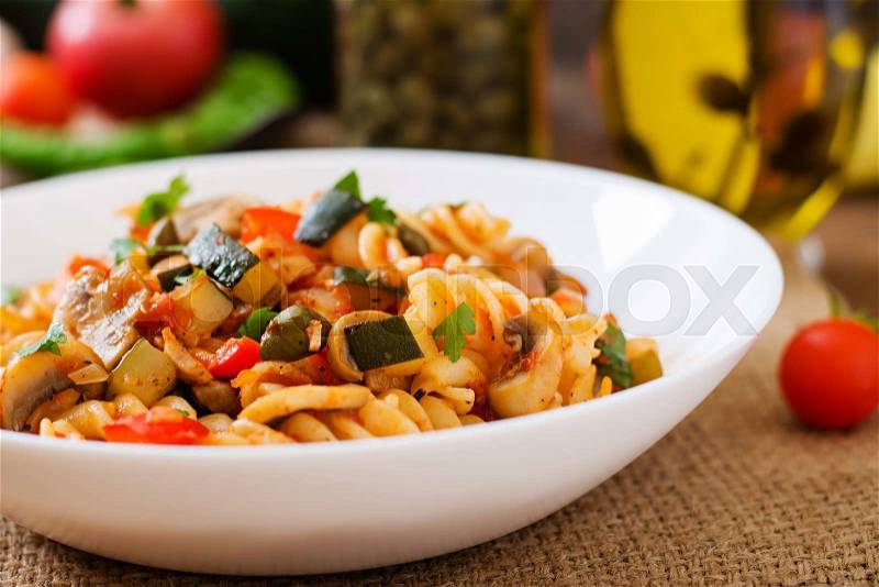 Vegetarian Vegetable pasta Fusilli with zucchini, mushrooms and capers in white bowl on wooden table, stock photo