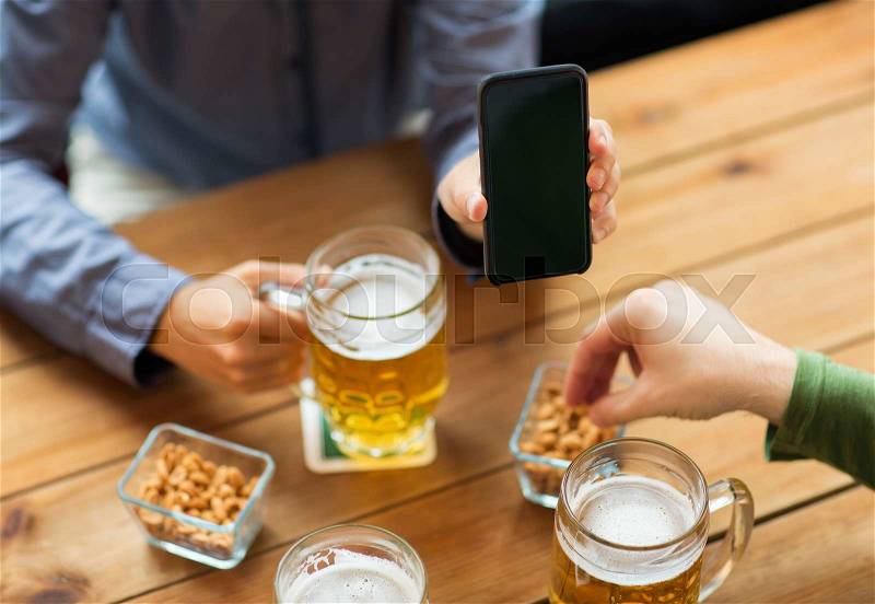 People, leisure, friendship and technology concept - close up of two male friends drinking beer with snacks and showing smartphone black blank screen at bar or pub, stock photo