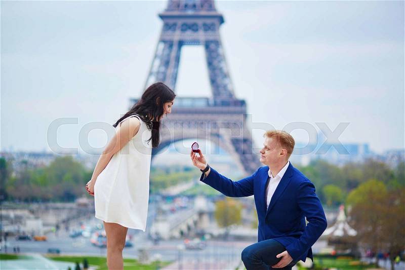 Romantic engagement in Paris, man proposing to his beautiful girlfriend near the Eiffel tower. Surprise proposal or elopement concept, stock photo
