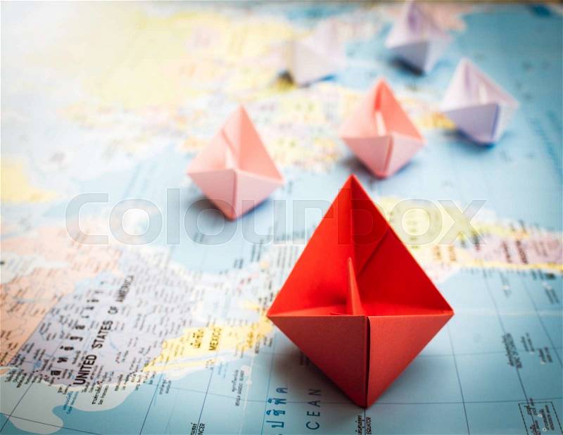 Paper boats following a red leader boat on world map. Concept for leadership, teamwork and winning success, stock photo