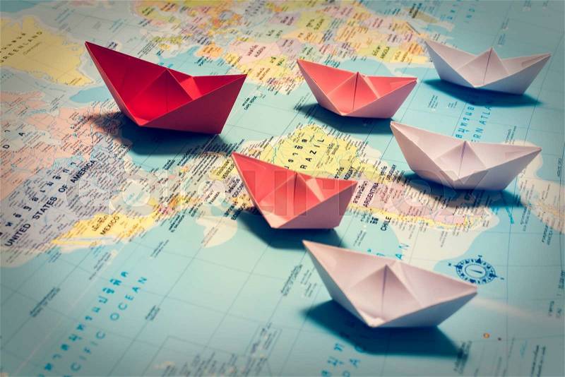 Paper boats following a red leader boat on world map. Concept for leadership, teamwork and winning success, stock photo