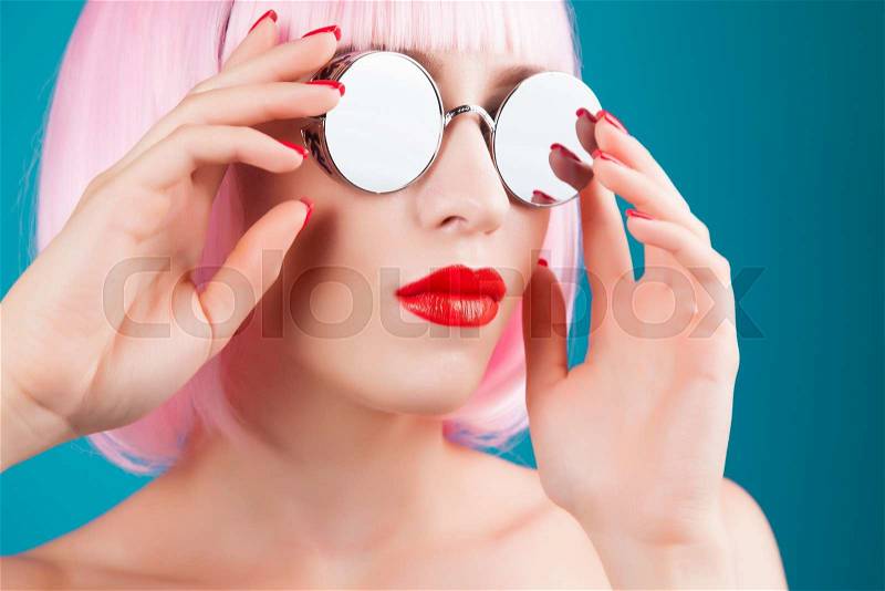 Beautiful woman wearing colorful wig and silver sunglasses against blue background, stock photo