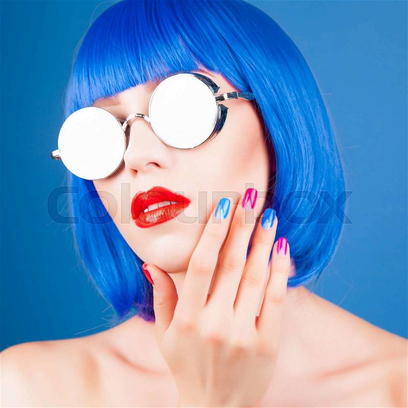 Beautiful woman wearing colorful wig and silver sunglasses against blue background, stock photo