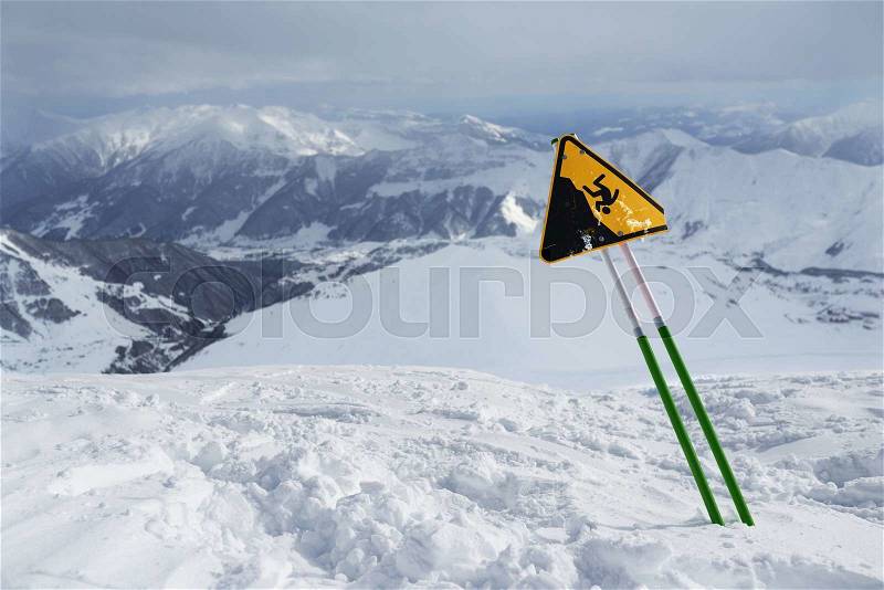 Label warning of a sharp cliff, standing in the snowy mountains, stock photo