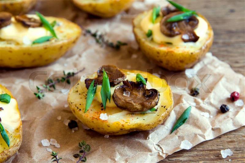 Baked potatoes with mushroom, cheese, greens and sea salt on paper and rustic wooden background close up, stock photo