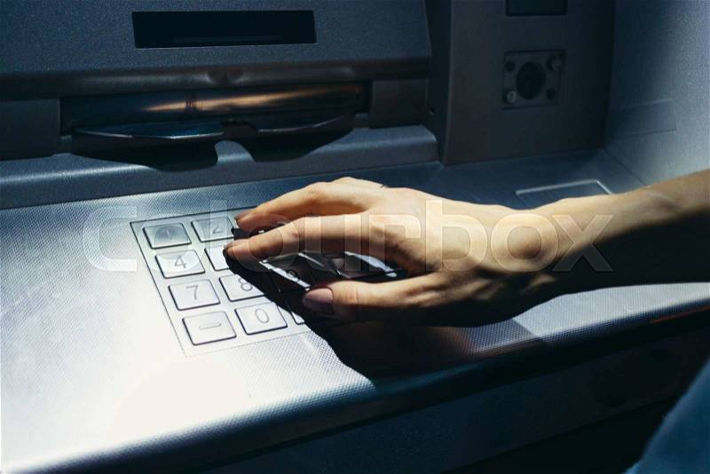 Woman\'s hand enters the secret code at the ATM on the street at night, stock photo